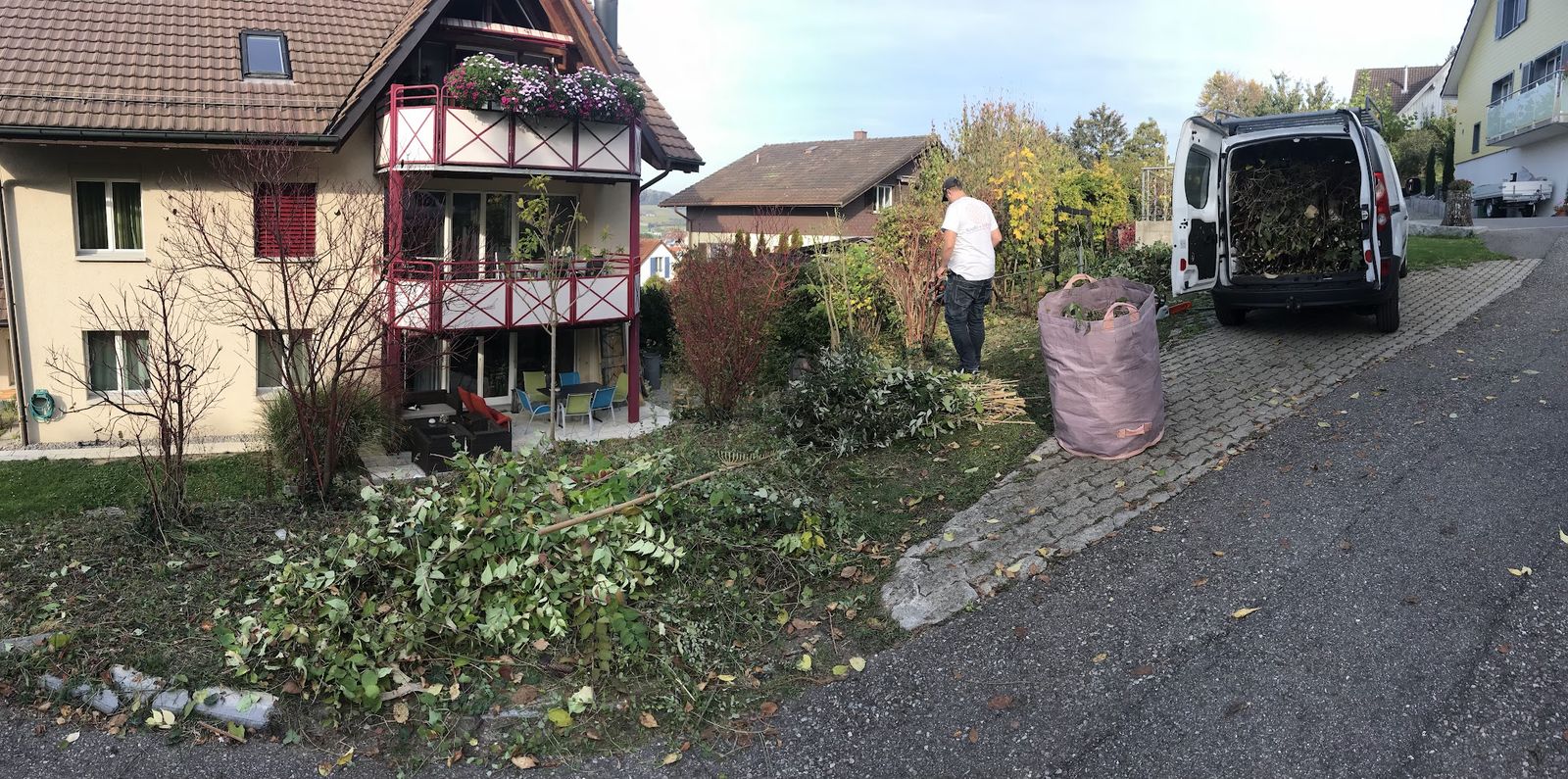 Gartenarbeit bei einem Wohnhaus, Schnittgut und Firmenbus an der Strasse